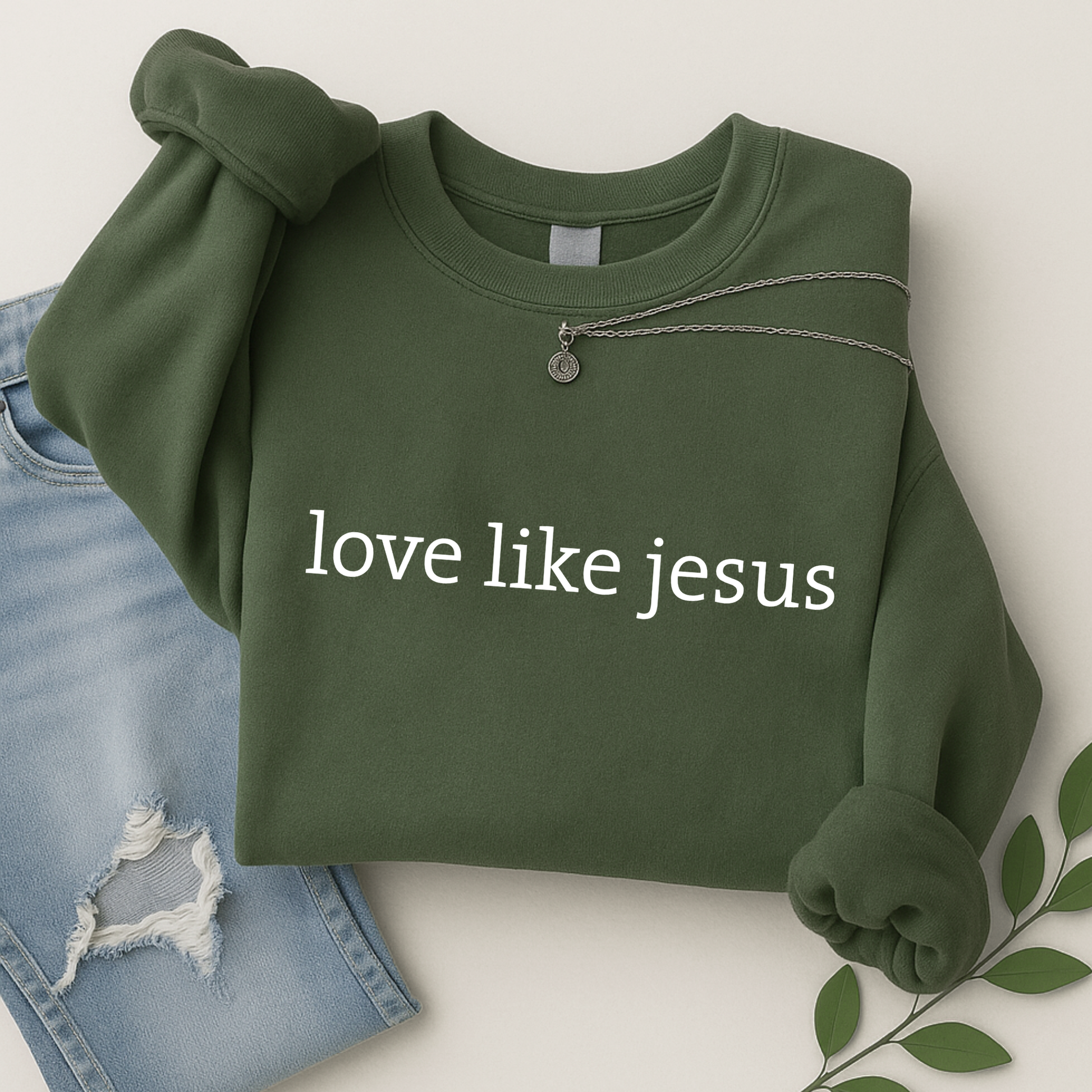 Folded green “Love Like Jesus” sweatshirt with jeans and jewelry