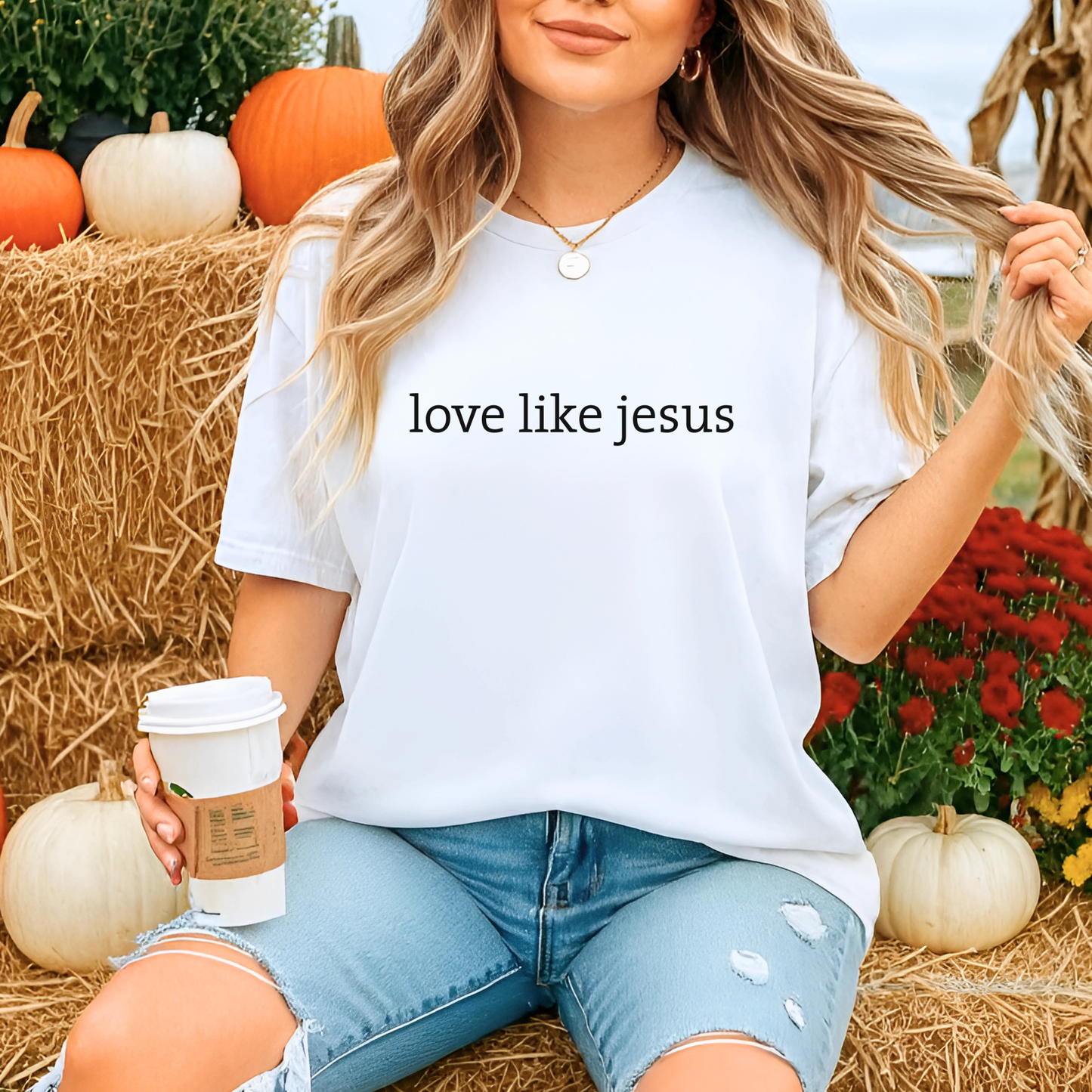 Woman wearing white “Love Like Jesus” minimalist tee at pumpkin patch with coffee