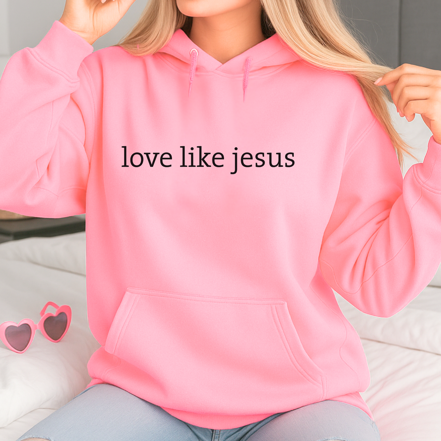 Lifestyle image of woman wearing bright pink hoodie with “love like jesus” text while seated indoors