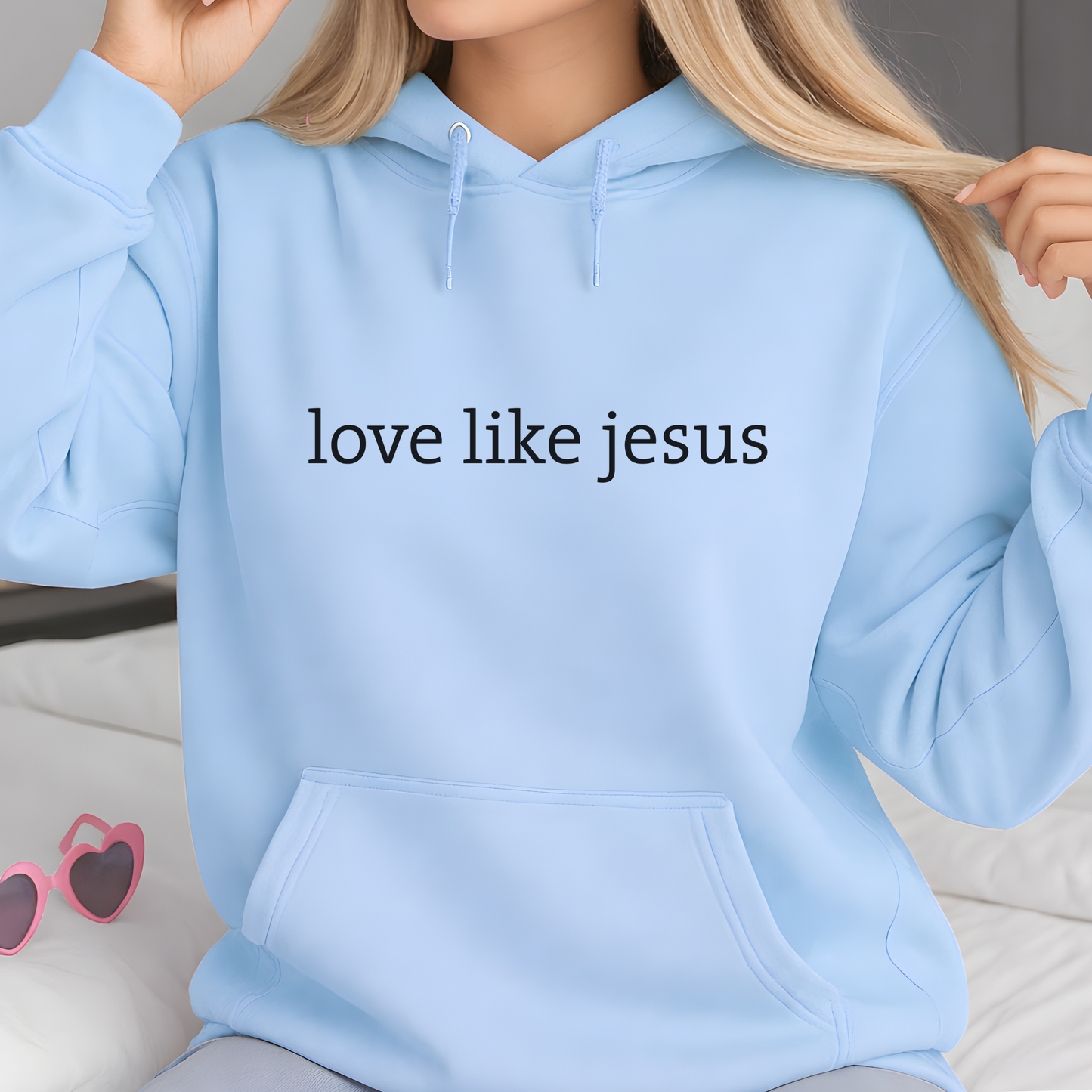 Lifestyle image of woman wearing light blue hoodie featuring “love like jesus” minimalist text