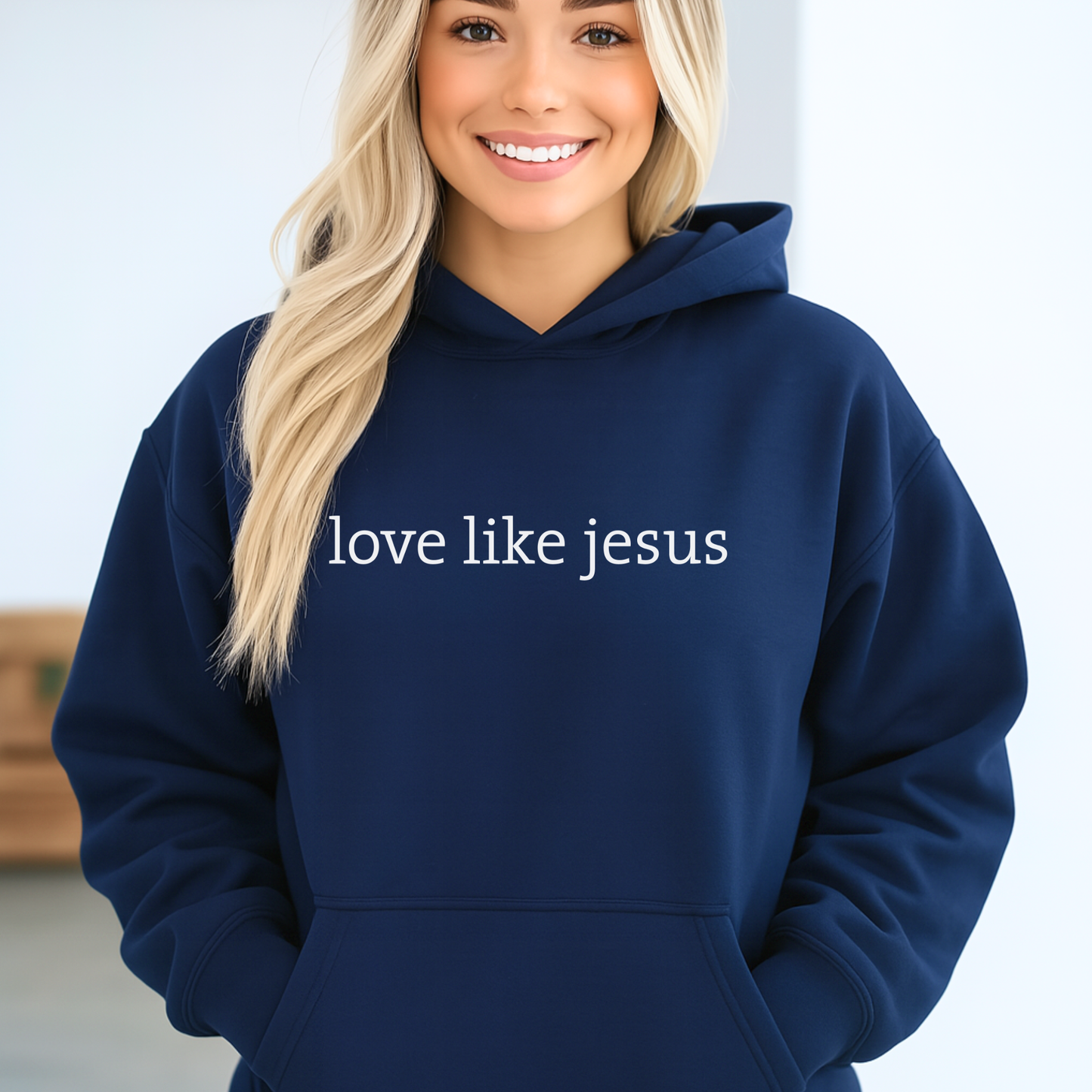 Lifestyle image of woman wearing navy hoodie with “love like jesus” text and hands in pocket