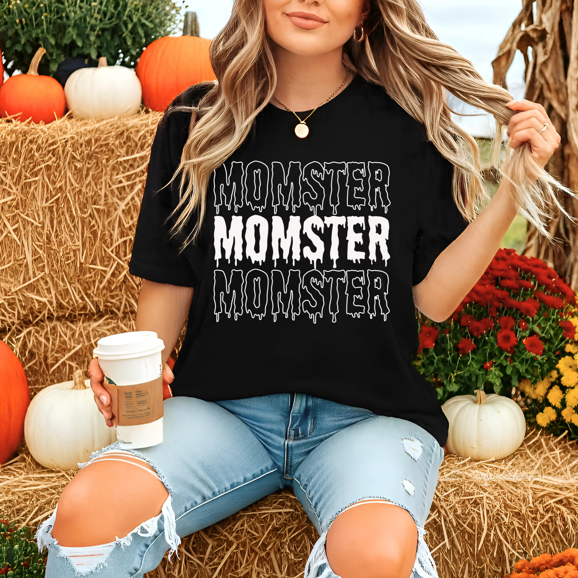 Person wearing a black t-shirt with 'Momster' text, holding a coffee cup, surrounded by pumpkins and flowers.