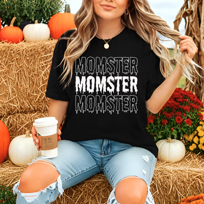 Person wearing a black t-shirt with 'Momster' text, holding a coffee cup, surrounded by pumpkins and flowers.