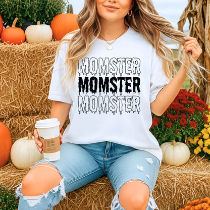 Woman wearing a 'Momster' shirt in a Halloween-themed setting with pumpkins and hay.