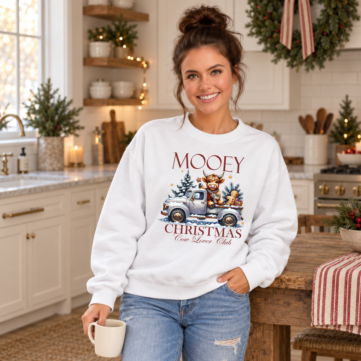Woman wearing a white Mooey Christmas cow graphic sweatshirt in a festive kitchen.