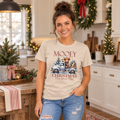 Woman wearing a sand T-shirt with Mooey Christmas Highland cow and truck graphic in a festive kitchen.