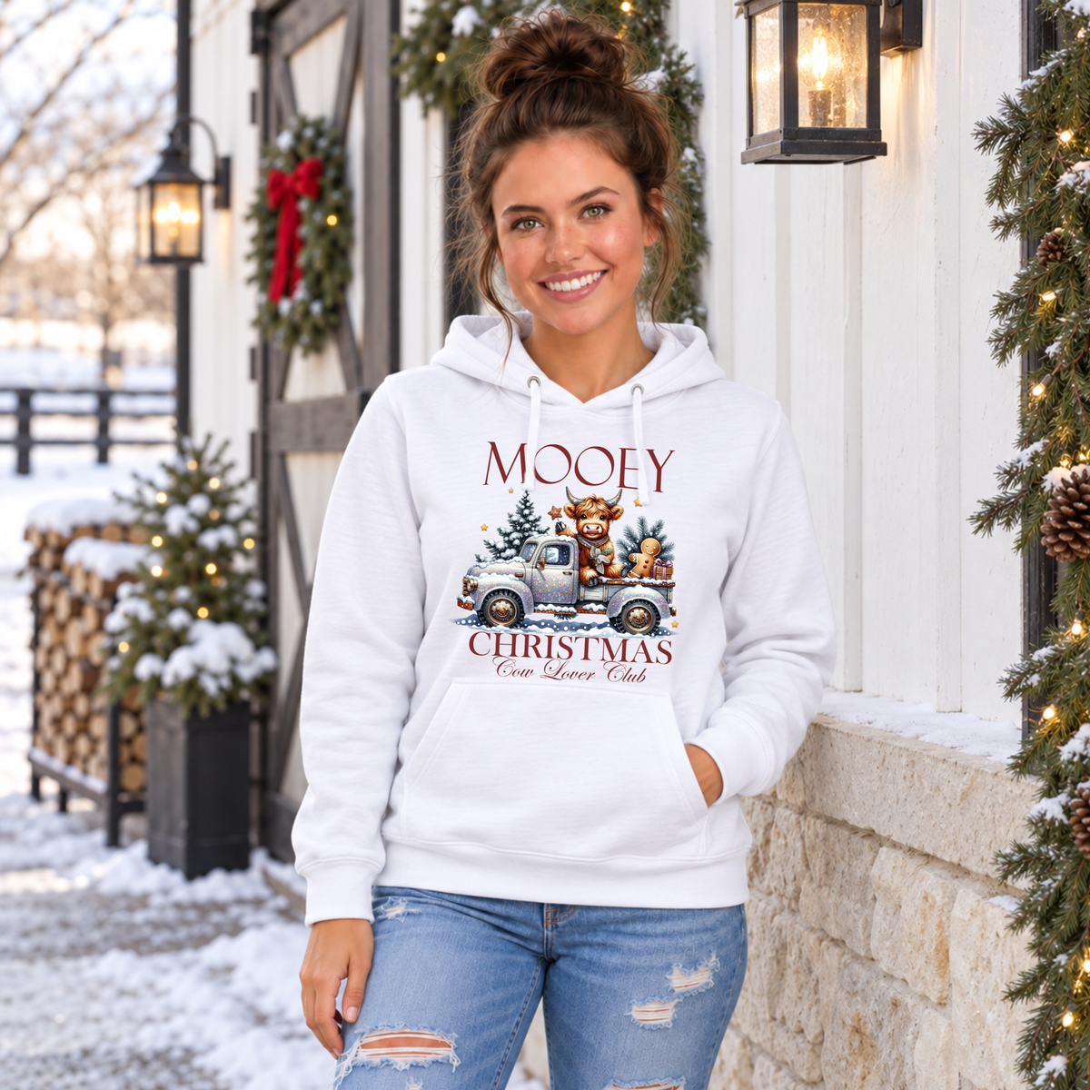 Woman wearing a white Mooey Christmas cow graphic hoodie outside a snowy holiday storefront.