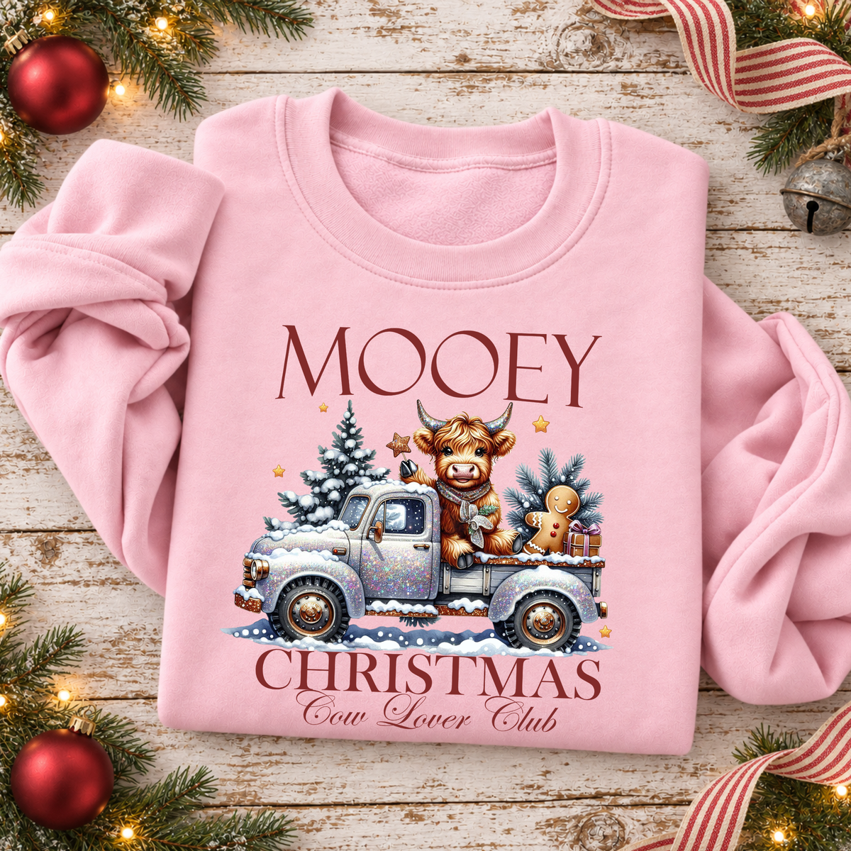 Pink sweatshirt flat lay with Mooey Christmas Cow Lover Club graphic showing a Highland cow in a snowy vintage truck.