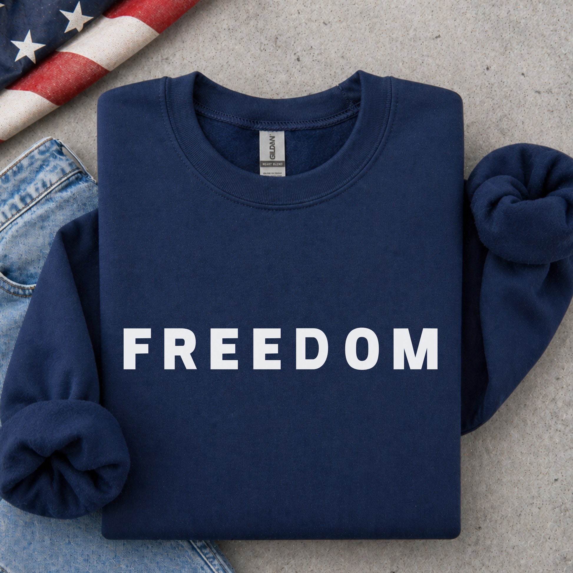 Navy blue sweatshirt with 'FREEDOM' text on a concrete surface with jeans and an American flag.