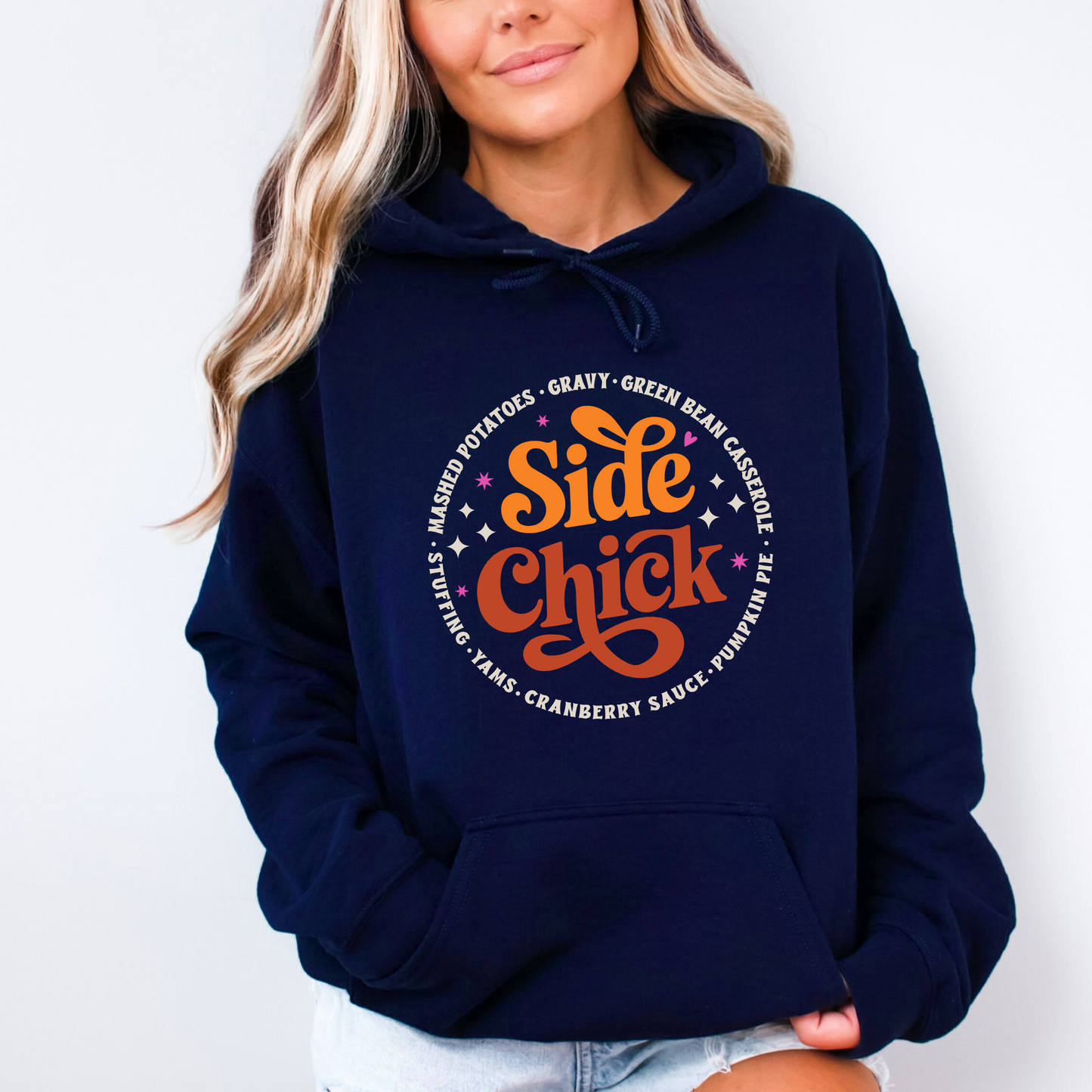 Navy blue “Side Chick” hoodie worn by woman with blonde hair and rolled sleeves. Retro fall graphic surrounded by classic Thanksgiving sides. Ideal for cool-weather gatherings and seasonal outfits.