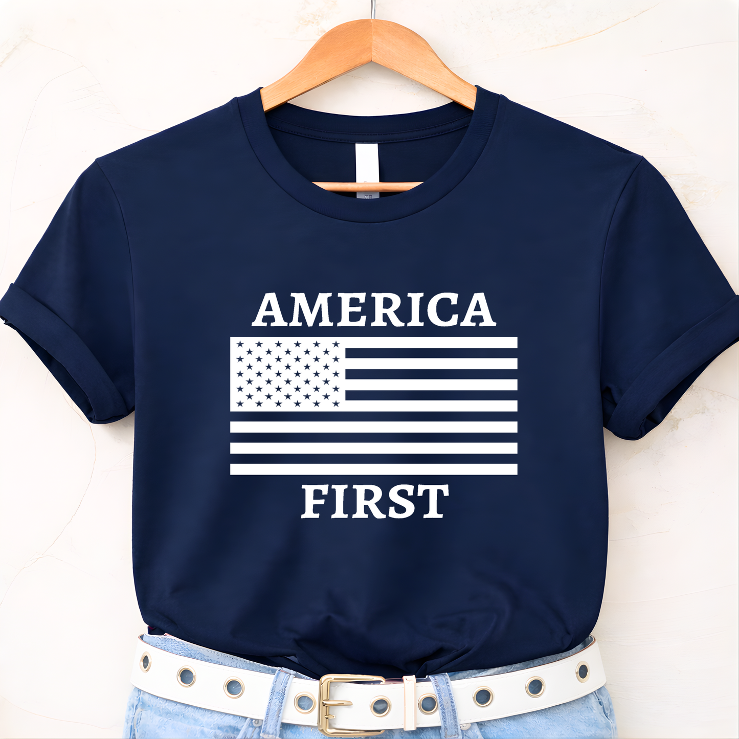 Navy blue t-shirt with 'AMERICA FIRST' graphic on a hanger against a white background