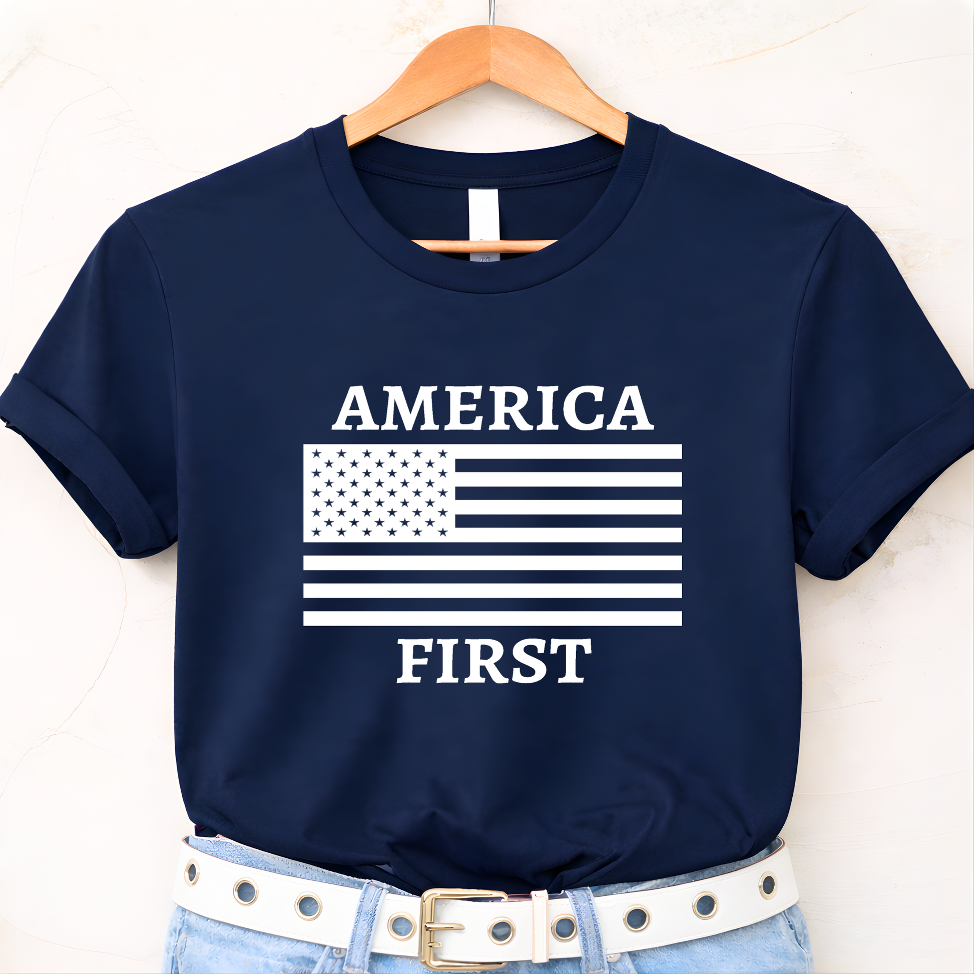 Navy blue t-shirt with 'AMERICA FIRST' graphic on a hanger against a white background