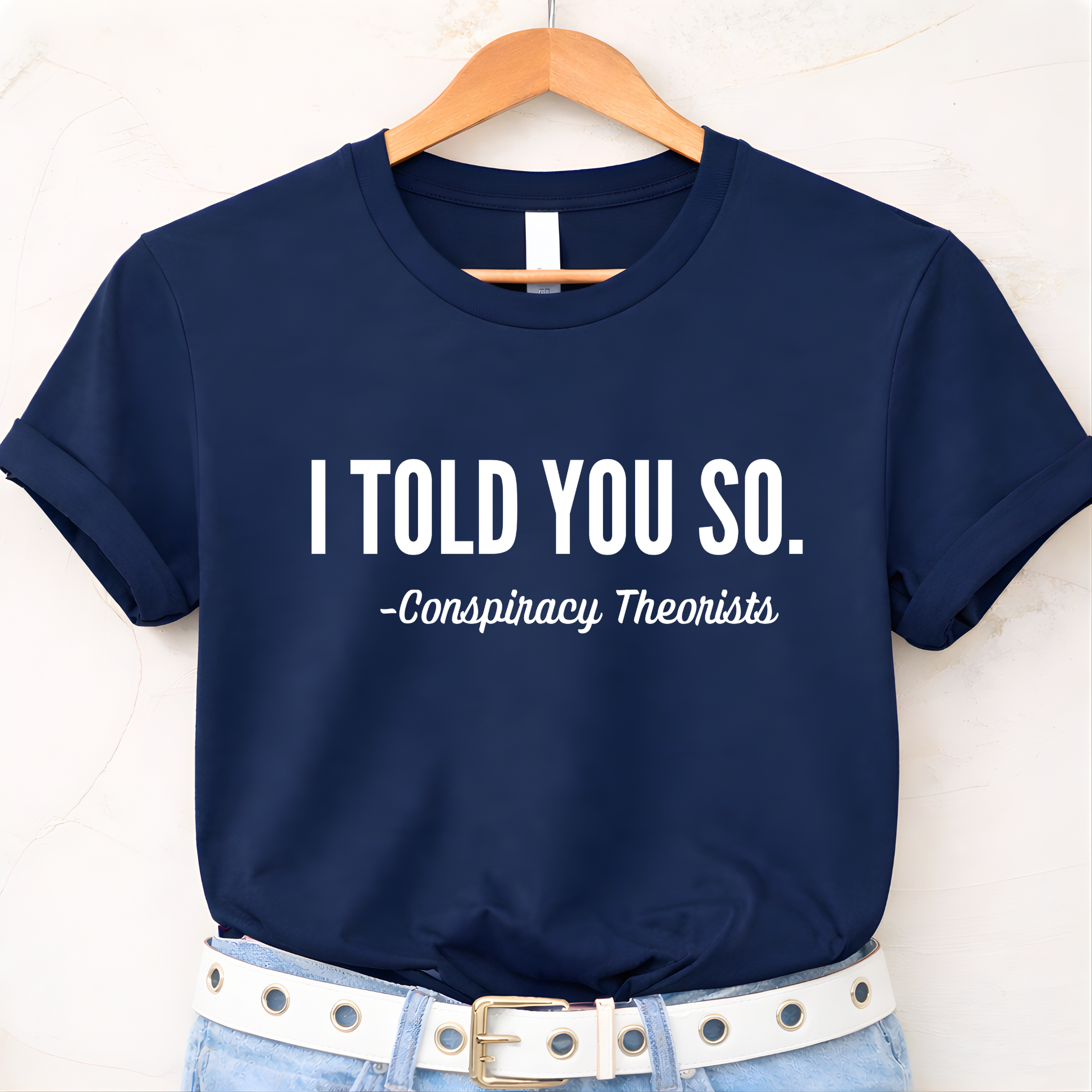 Navy blue t-shirt with 'I Told You So. - Conspiracy Theorists' text on a hanger.