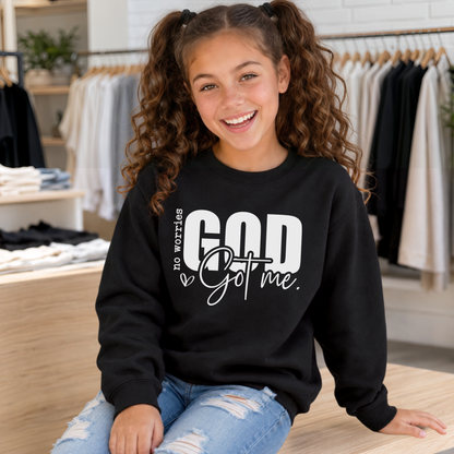 Youth model wearing a black No Worries God Got Me crewneck sweatshirt with bold white lettering in a boutique setting.