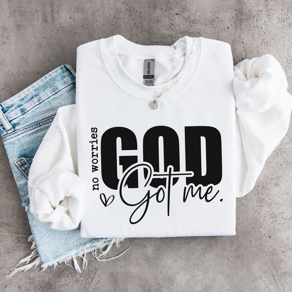 White No Worries God Got Me youth crewneck sweatshirt flat lay with bold black lettering styled with denim.