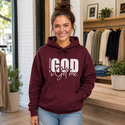 Woman wearing a maroon No Worries God Got Me hoodie with bold white graphic lettering inside a boutique.