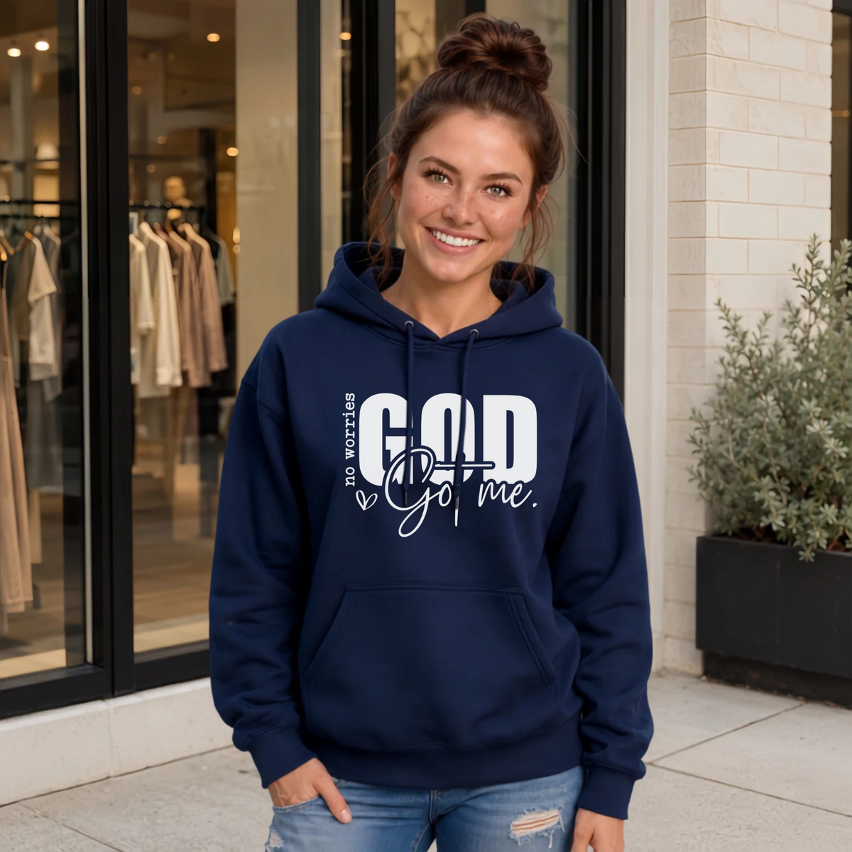 Woman wearing a navy No Worries God Got Me hoodie with bold white graphic lettering outside a boutique.