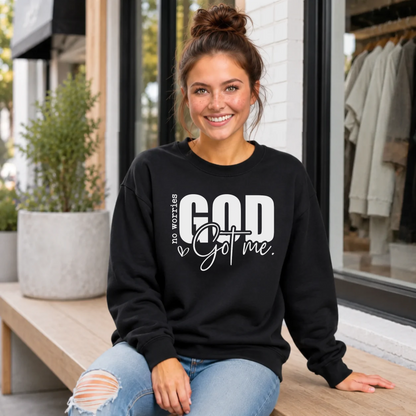 Woman wearing a black No Worries God Got Me crewneck sweatshirt with bold white graphic lettering while seated outside.