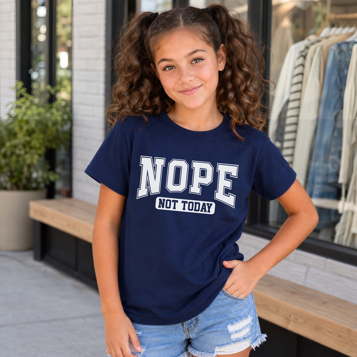 Youth model outside a boutique in a Navy T-shirt with white NOPE NOT TODAY varsity lettering.