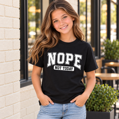 Youth model wearing a black NOPE NOT TODAY T-shirt with white lettering beside a brick cafe entrance.