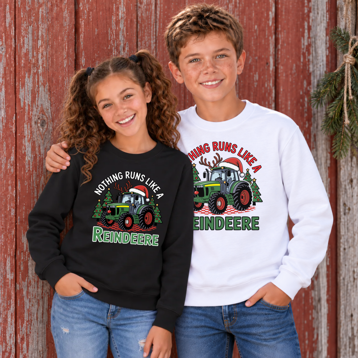 Boy in a white Christmas tractor sweatshirt with a girl in a black sweatshirt in front of a weathered red barn.