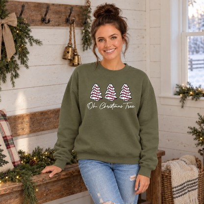 Woman wearing a military green Oh Christmas Tree sweatshirt beside a decorated bench and snowy window.