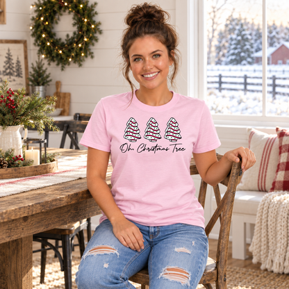 Woman wearing a light pink Oh Christmas Tree T-shirt at a holiday dining table with snowy scenery outside.
