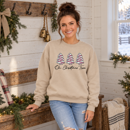 Woman wearing a sand Oh Christmas Tree sweatshirt beside a wooden bench and Christmas greenery.