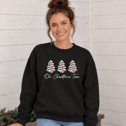 Woman wearing a black Oh Christmas Tree sweatshirt with three decorated tree shapes against a white wood wall.