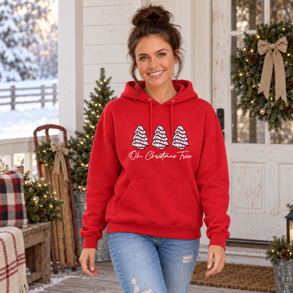 Woman in a red Oh Christmas Tree hoodie on a porch with a wreath and snowy background.