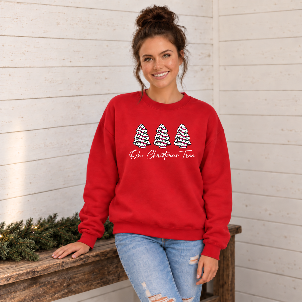 Woman wearing a red Oh Christmas Tree sweatshirt against a white wood wall with Christmas greenery.