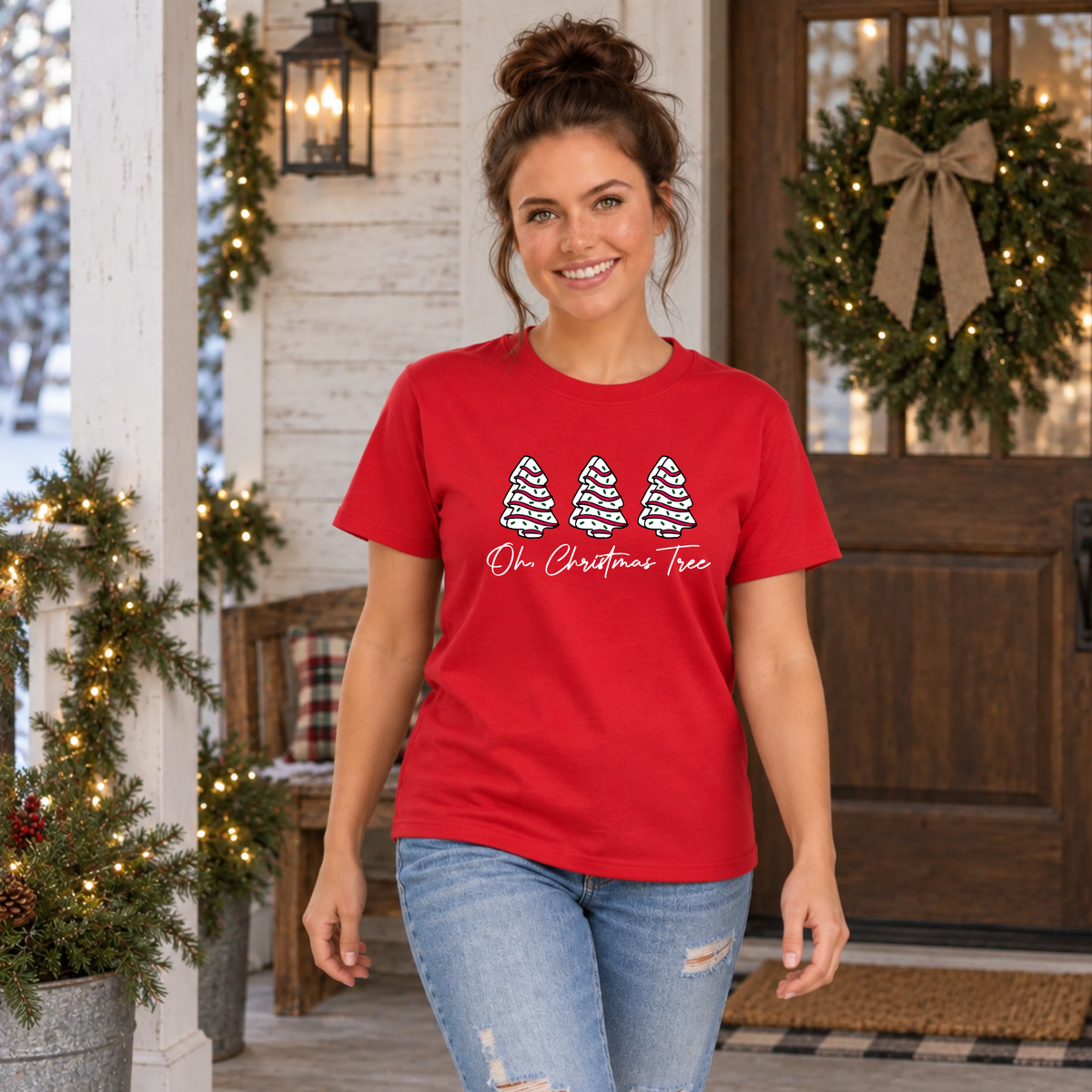 Woman in a red Oh Christmas Tree T-shirt by a front door with a lit wreath.