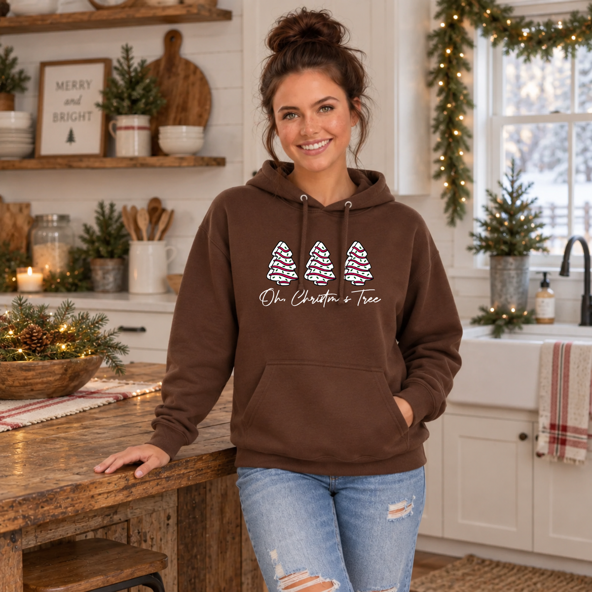Woman wearing a brown Oh Christmas Tree hoodie at a rustic kitchen island with Christmas decorations.