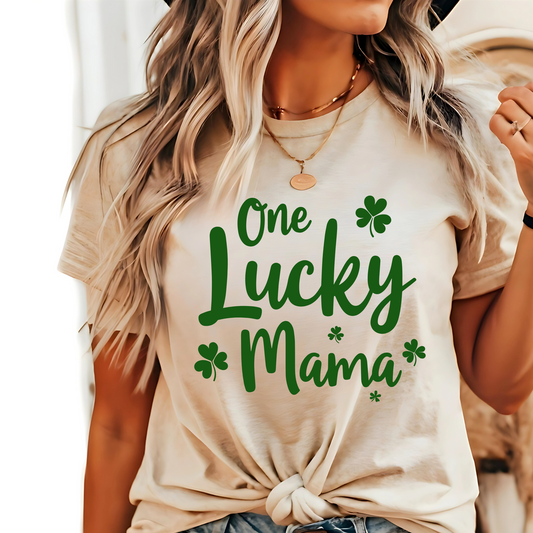 A stylish sand t-shirt with "One Lucky Mama" in green script, decorated with shamrocks. Perfect for moms celebrating St. Patrick’s Day in a cute and festive way.