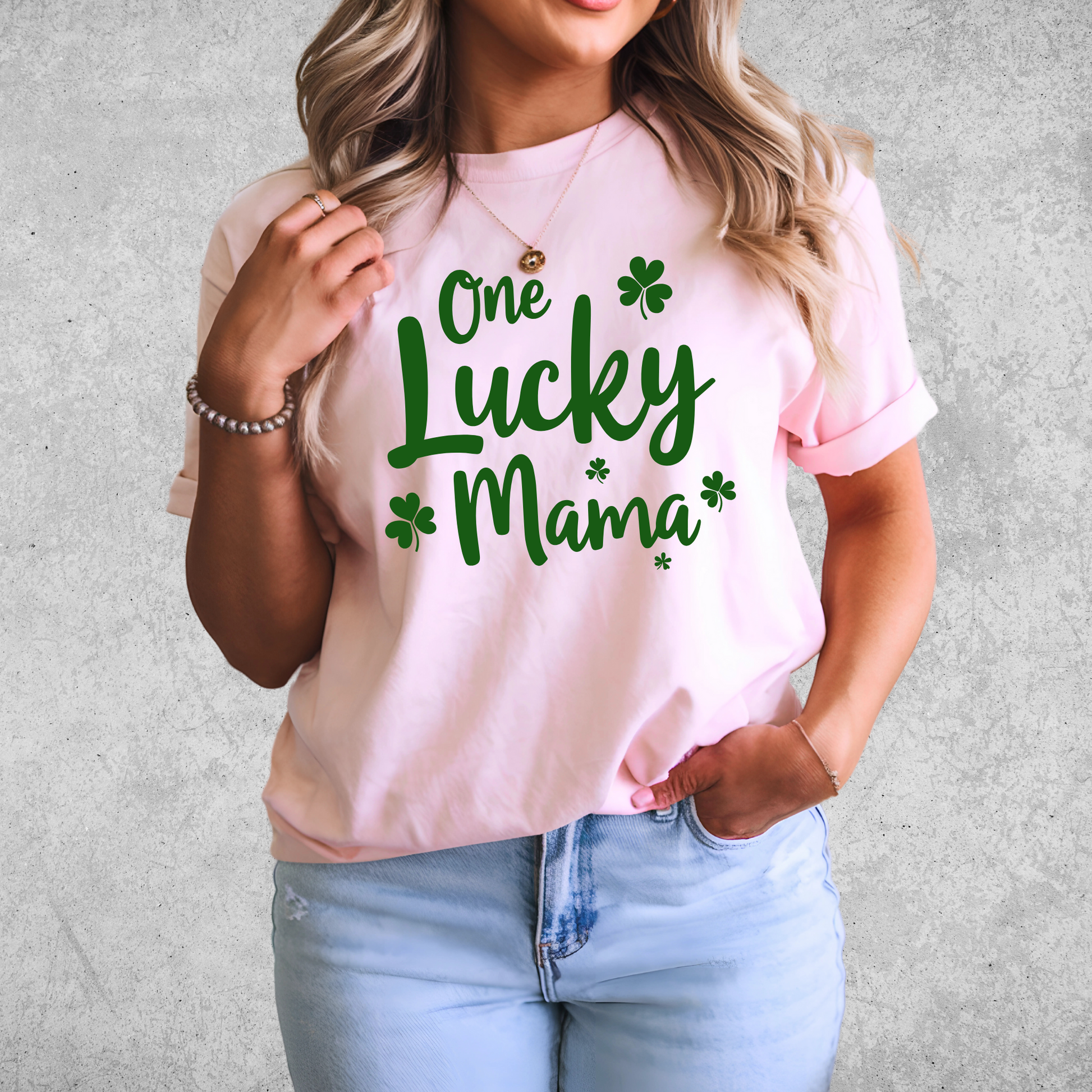 A stylish pink t-shirt with "One Lucky Mama" in green script, decorated with shamrocks. Perfect for moms celebrating St. Patrick’s Day in a cute and festive way.