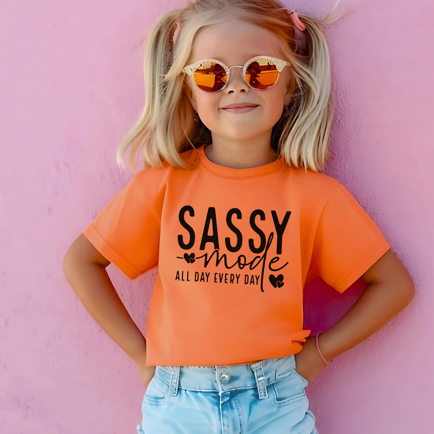 Young girl wearing a Orange 'Sassy Mode – All Day Every Day' graphic t-shirt, smiling confidently outdoors