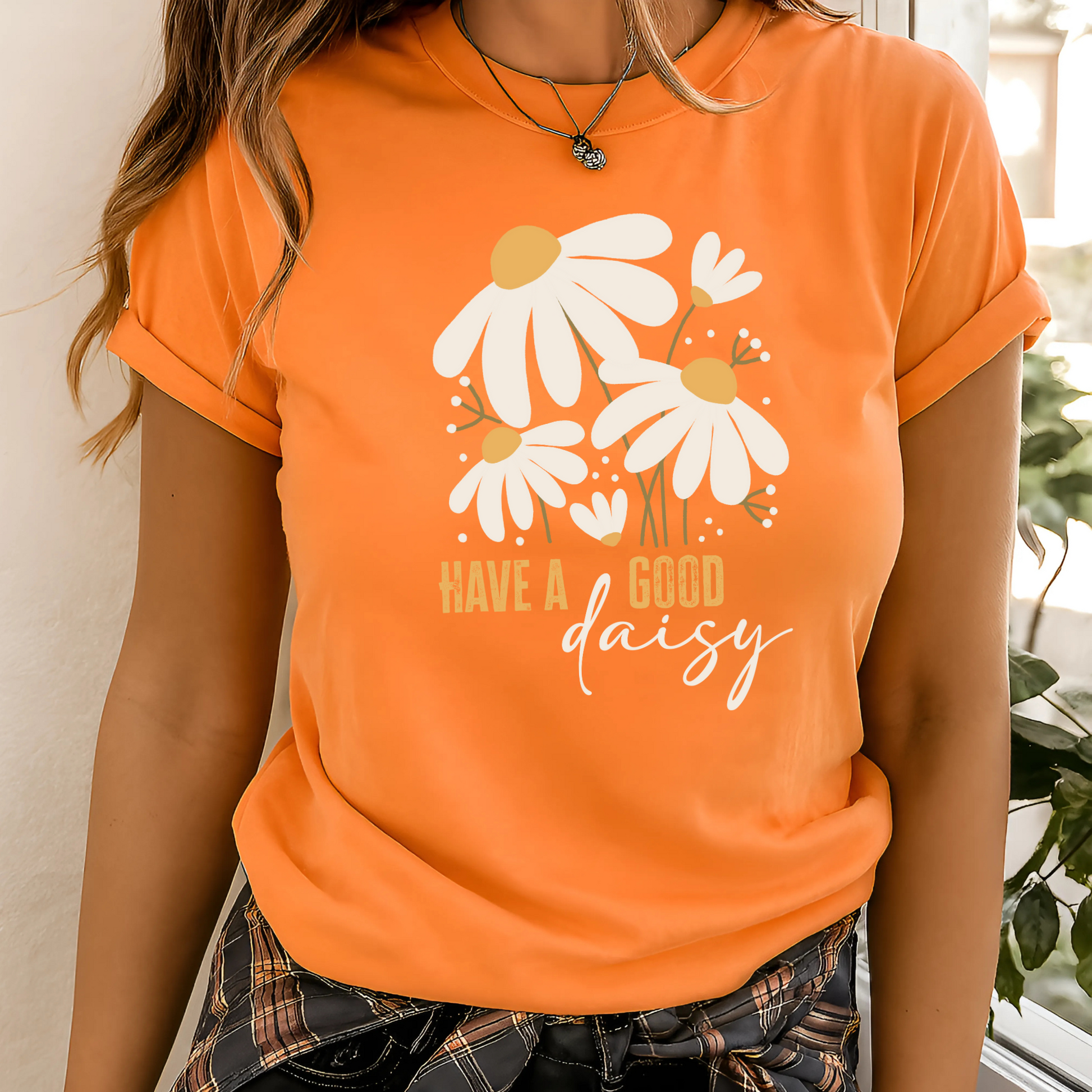 Orange “Have a Good Daisy” T-shirt with white daisy graphic and retro lettering, styled for fall with warm tones and seasonal outfit layering.