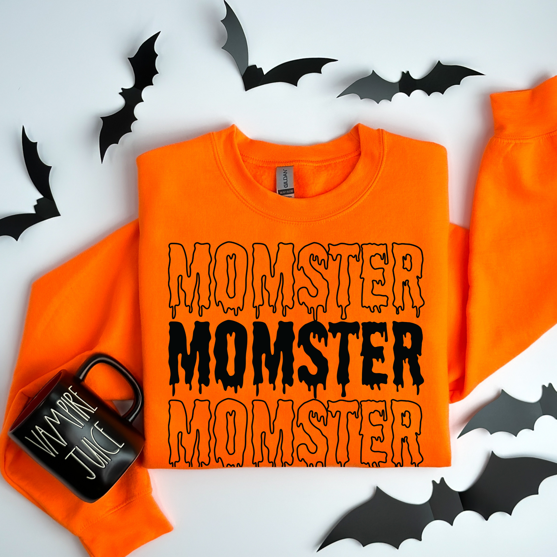 Orange sweatshirt with 'MONSTER' text and a black mug on a white background with bats.