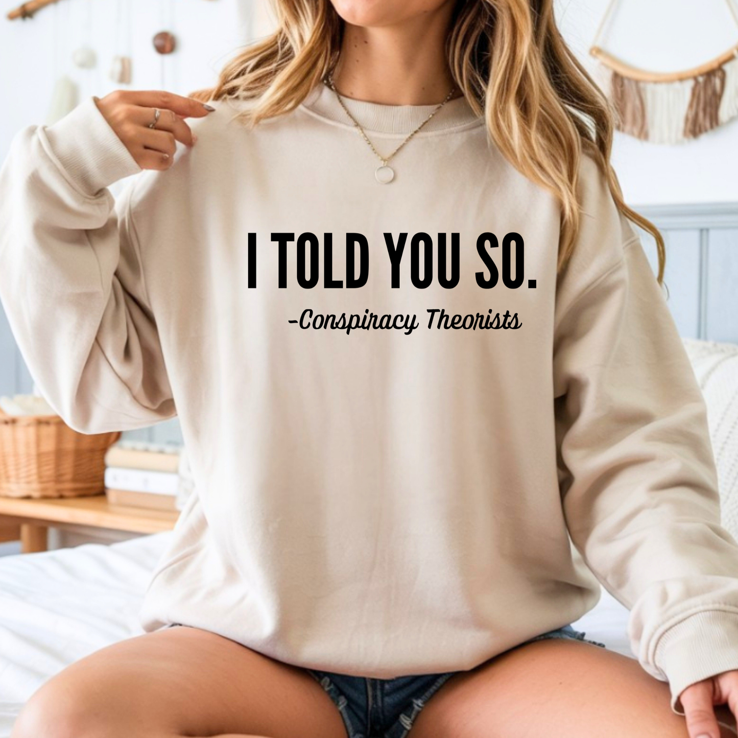 Person wearing a beige sweatshirt with text 'I Told You So. - Conspiracy Theorists' in a casual setting.