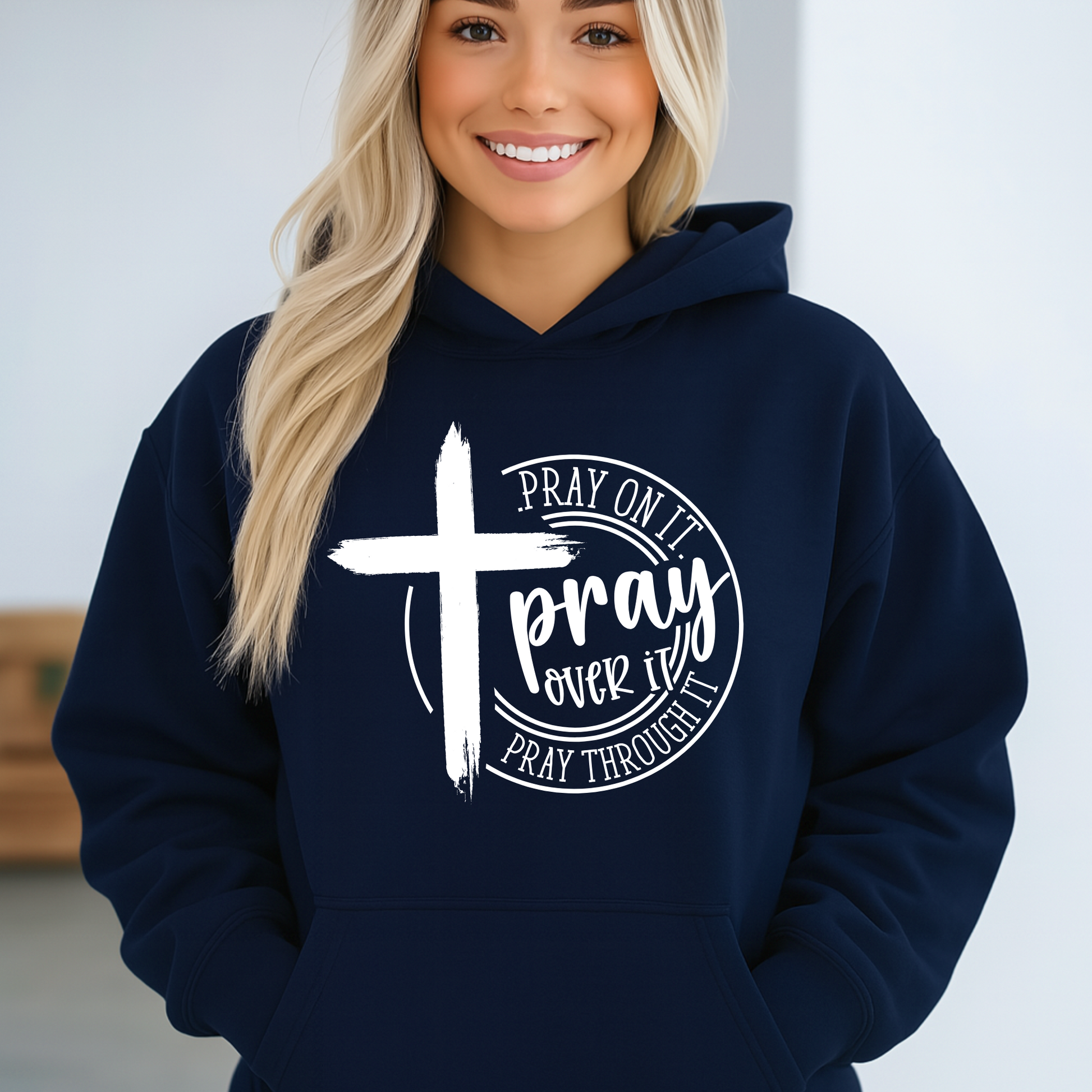 Person wearing a navy hoodie with a cross and text design on a plain background