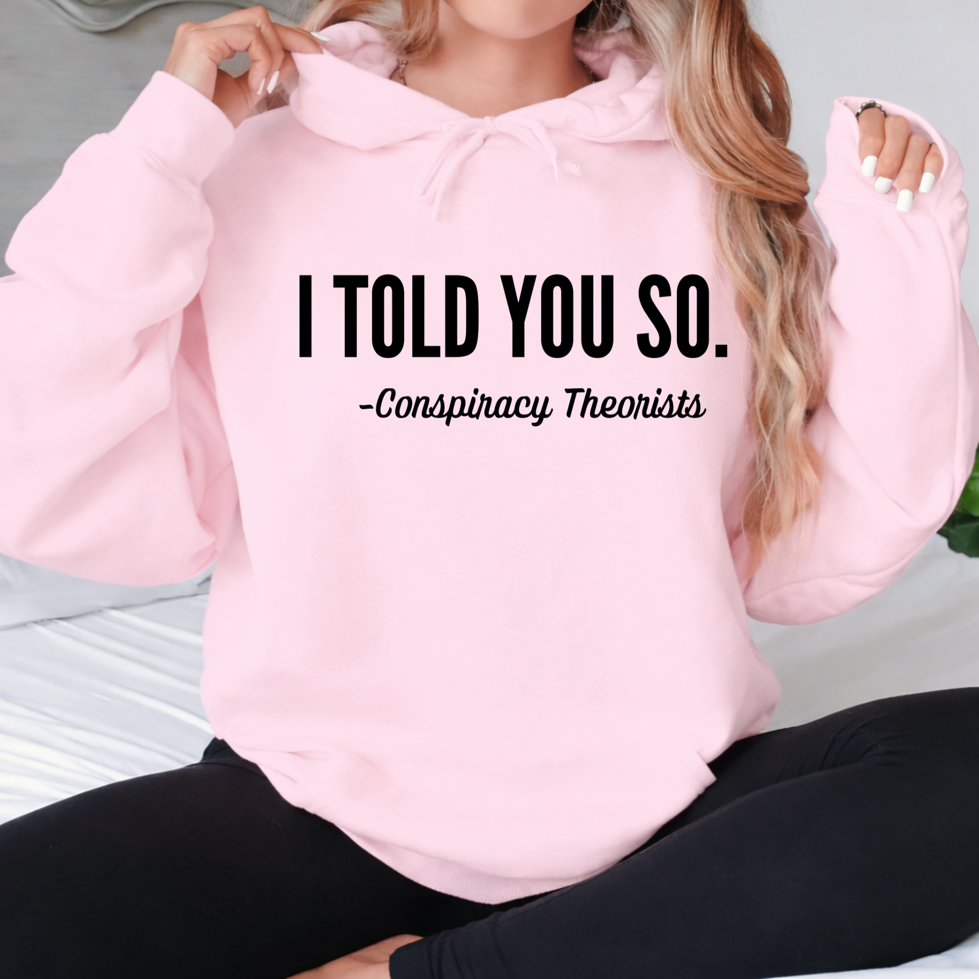 Person wearing a pink hoodie with text 'I TOLD YOU SO. - Conspiracy Theorists' on a light background