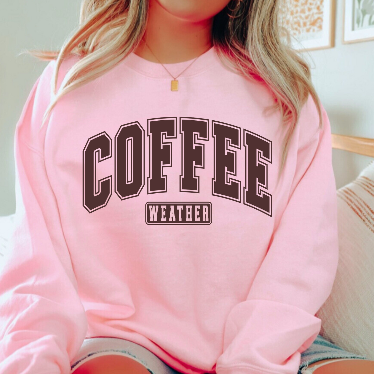 Pink sweatshirt styled with “Coffee Weather” design, seated casually
