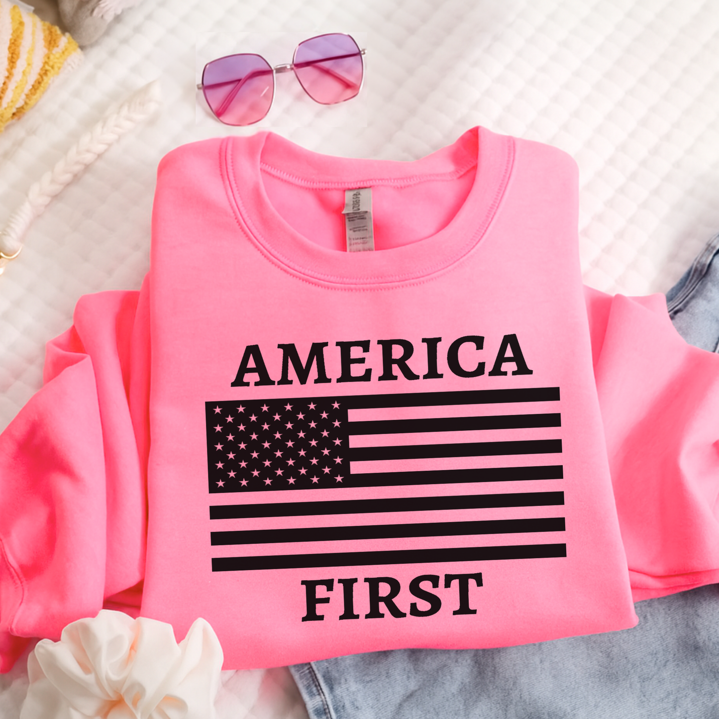 Pink sweatshirt with 'AMERICA FIRST' text and American flag design on a textured surface.