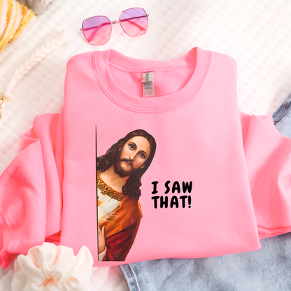 Pink sweatshirt with a graphic of a jesus saying  'I saw that!' text, placed on a textured surface.