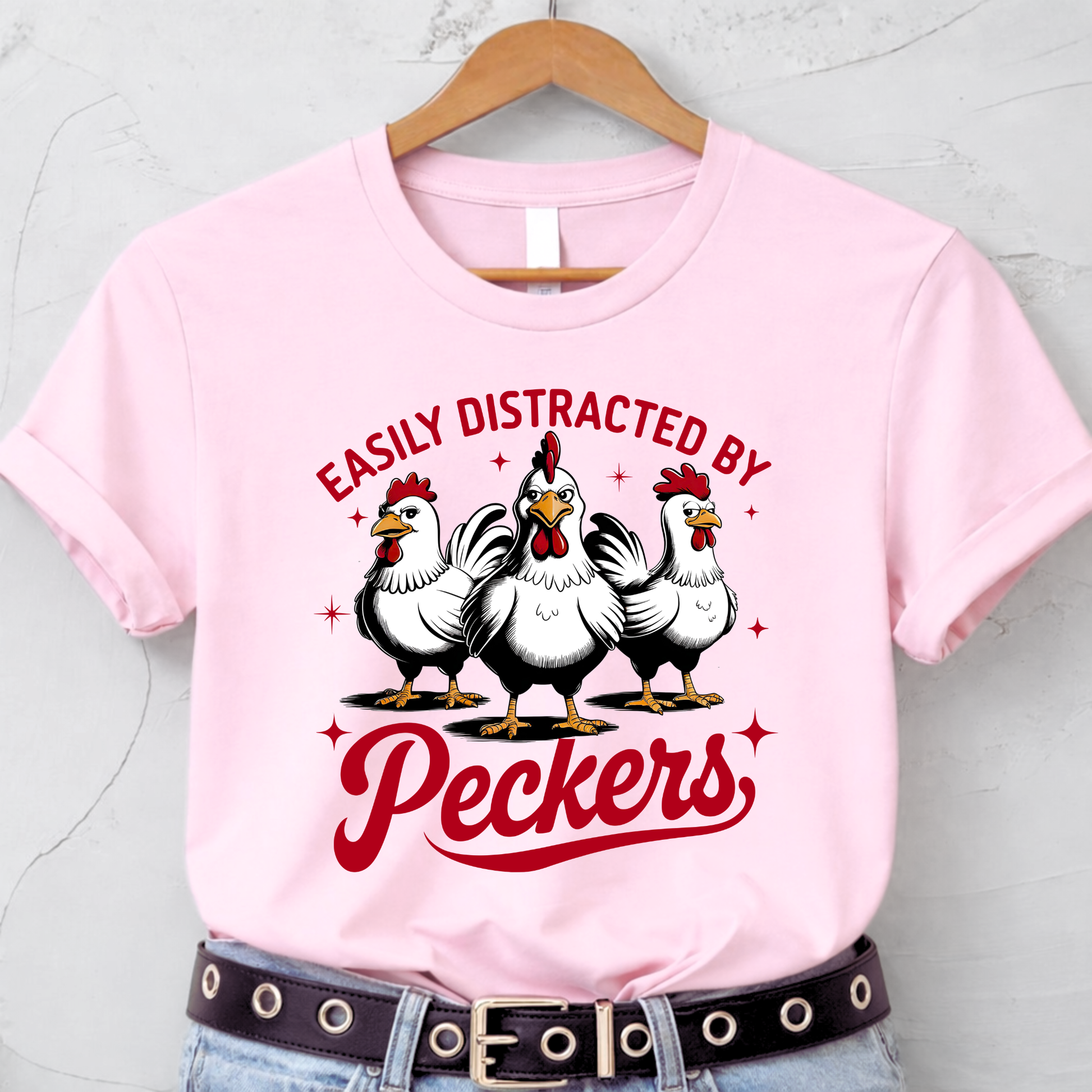 Pink t-shirt with chicken graphic and text on a hanger against a light gray background