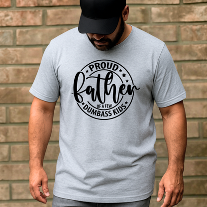 Man wearing a gray t-shirt with 'Proud Father of a Few Dumbass Kids' text against a brick wall.