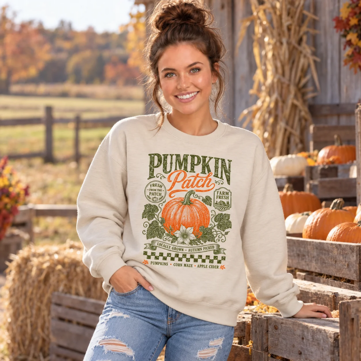 Woman wearing a sand sweatshirt with vintage Pumpkin Patch pumpkin and floral design beside pumpkins at a fall farm