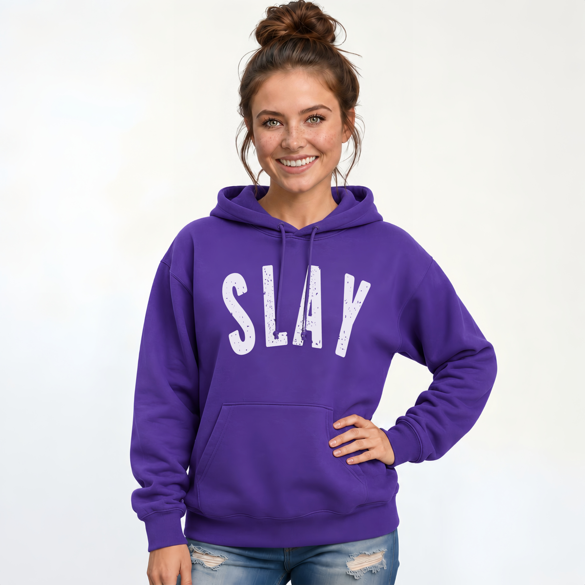 Woman wearing a purple SLAY hoodie with bold white distressed lettering against a white studio background.