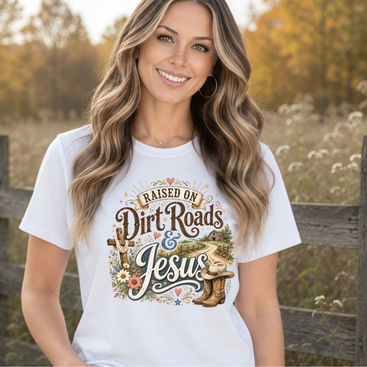 Woman wearing a white Raised on Dirt Roads & Jesus T-shirt in a warm country field setting.