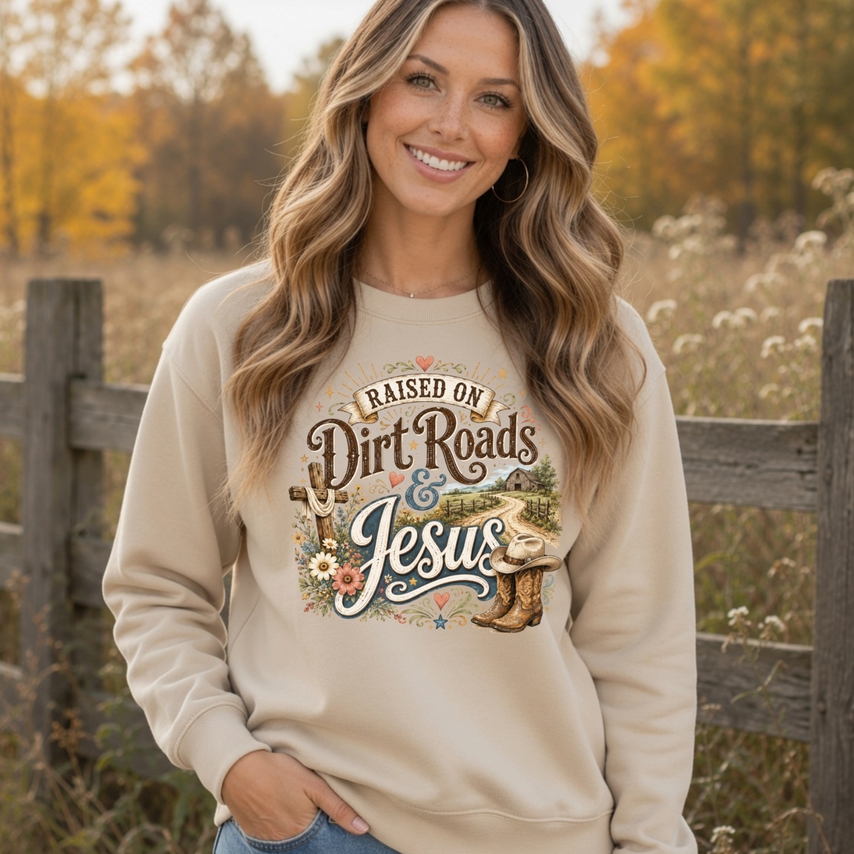 Woman modeling a sand Raised on Dirt Roads & Jesus crewneck sweatshirt outdoors with autumn trees behind her.